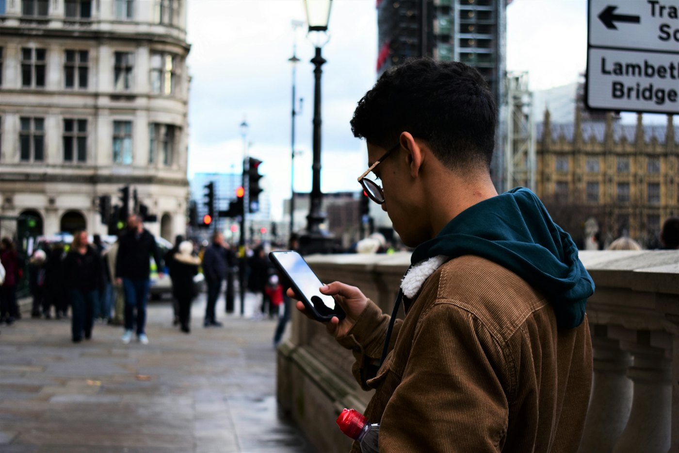Um homem em pé numa rua cheia de gente olha para o celular